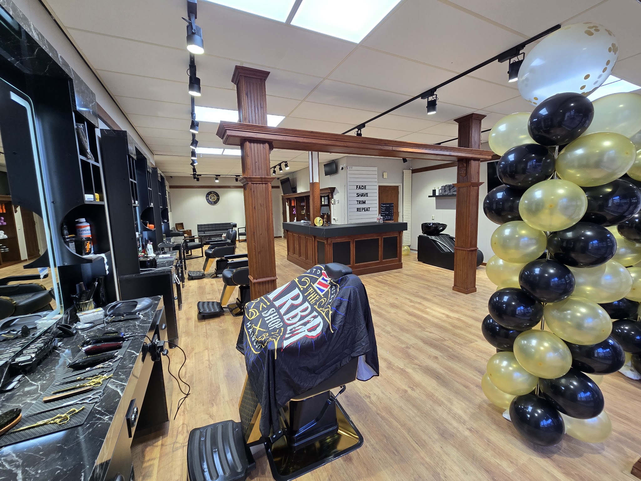 De barbershop van binnen: zwarte werkplekken met marmer, een barbiersstoel, houten zuilen en de balie achterin